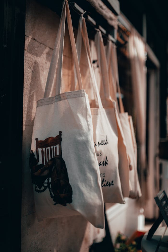 our-mission-01 Close-up of canvas tote bags hanging on a rack in a warmly lit store interior.